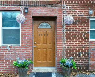 a brick house with a wooden door and two plants at Cozy studio at the heart of Jackson Heights in Queens