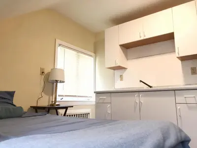a bedroom with a bed and a kitchen with a window at 1950s Charm In The Heart Of Waterbury in Waterbury