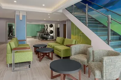 a lobby with chairs and tables and a staircase at Holiday Inn Express & Suites Woodside LaGuardia Airport in Queens
