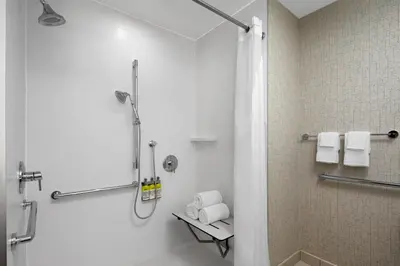 a bathroom with a shower and a sink with towels at Holiday Inn Express & Suites Woodside LaGuardia Airport in Queens