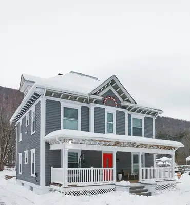 a gray house with a red door in the snow at Chateau Lodge - Ski Shandaken, Hunter, Catskills, Windham, Belleayre in Shandaken