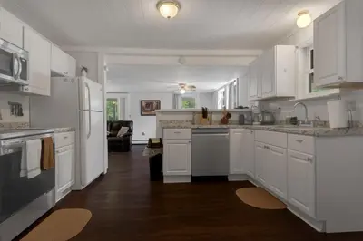 a white kitchen with white cabinets and a living room at Two Brooks Lodge in Bennington