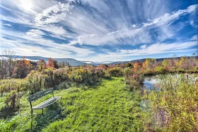 a park bench sitting on a hill next to a river at Full Private Home on 32-Acres with Stellar Views! in North Blenheim