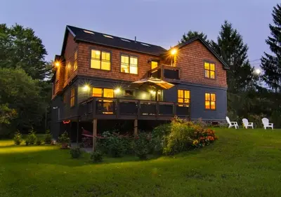 a large house with lights on in a yard at Too Good AKA 2 Goodrich St in Stockbridge