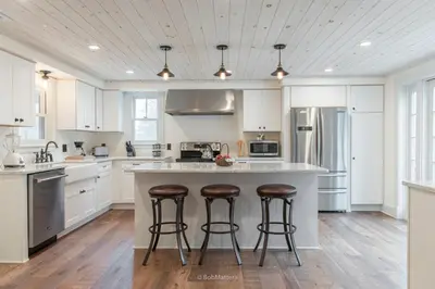 a kitchen with white cabinets and a large island with bar stools at Restored 1881 Farm House in Lenox