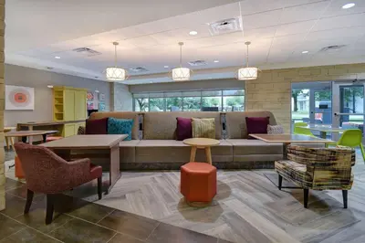 a waiting room with a couch and tables and chairs at Home2 Suites East Hanover, NJ in East Hanover