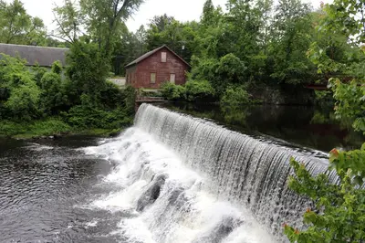a waterfall in front of a red building next to a river at Old Mill Inn in Hatfield