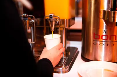 a person is pouring coffee into a cup at Wingate by Wyndham Bronx Haven Park in Bronx