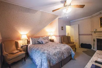 a bedroom with a bed and two chairs and a ceiling fan at Deerfield Valley Inn - Mt Snow BnB Fireplace Rooms and Breakfast in Dover