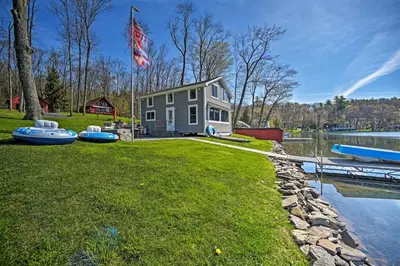 a house on the shore of a lake with a flag at BBQ Ready Lakeside Milford Home with Paddleboat in Milford