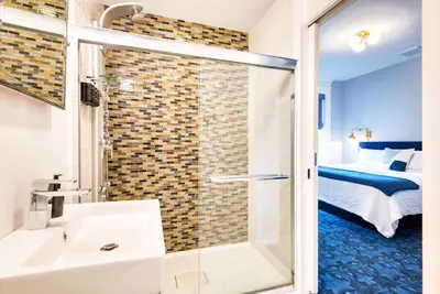 a bathroom with a shower and a sink and a bed at The Hudson Whaler in Hudson