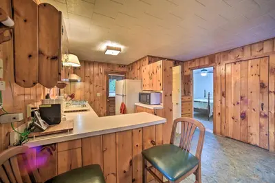 a kitchen with wooden walls and a counter and chairs at Riverfront Escape with Dock 19 Mi to Saratoga! in Lake Luzerne