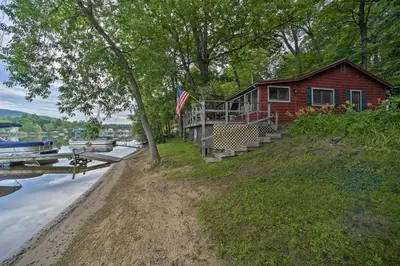 a house on the side of a river with a boat at Riverfront Escape with Dock 19 Mi to Saratoga! in Lake Luzerne