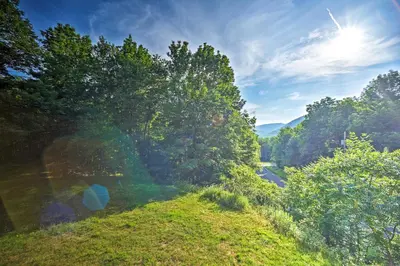 a grassy hill with trees on the side of a road at Modern Catskills Reprieve with Hot Tub and Mtn Views! in Margaretville