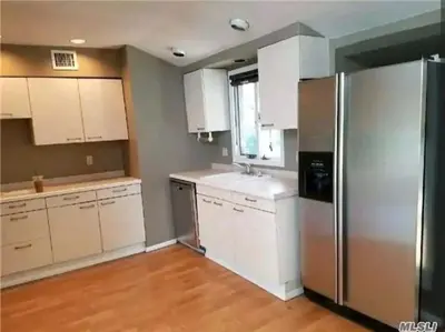 a kitchen with white cabinets and a stainless steel refrigerator at Cozy 4BR 3BA Home- Train to NYC, USOpen, CitiField Mets, MSG, Walk to Harbor & Golf in Port Washington