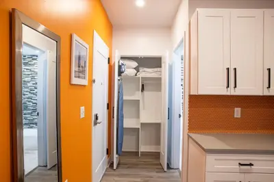a kitchen with white cabinets and an orange wall at Peachtree Suites - Jersey City in Jersey City