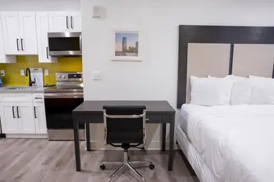 a bedroom with a desk and a bed and a kitchen at Peachtree Suites - Jersey City in Jersey City