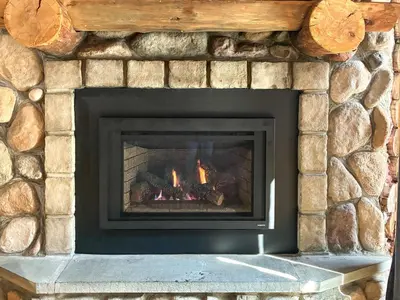 a stone fireplace with a fire in it at Pet-Friendly New York Cabin with Hot Tub and Game Room in Maplecrest