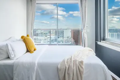 a white bed with a teddy bear on it in front of a window at The Modernist Hotel in Long Island City