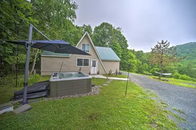 a house with a hot tub and an umbrella in the grass at A-Frame Cabin with Hot Tub 5 Mi to Waterford! in Melrose