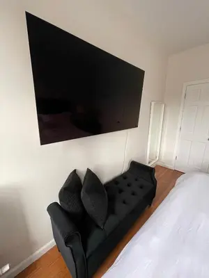 a bedroom with a black couch and a flat screen tv at 1BR Apt in Sunnyside 15 min to Manhattan in Woodside