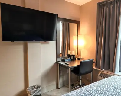 a hotel room with a desk and a large flat screen tv at Wheeler Hotel in Bronx