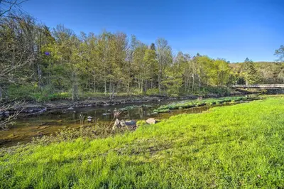 a river with green grass and a bridge in the background at half Mi to Windham Mtn Main Street Condo in Windham