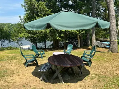a table and chairs under a green umbrella at Adirondack Waterfront Cabin Upper Hudson Tributary in Lake Luzerne