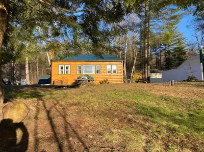 a small yellow house sitting in a yard at Adirondack Waterfront Cabin Upper Hudson Tributary in Lake Luzerne