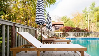 a deck with chairs and an umbrella next to a pool at 4BDR Heritage Estate w Pool Private Pond Fire Pit Cortland by AvantStay in Saugerties