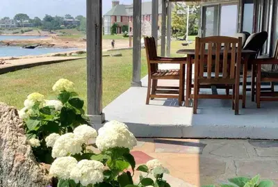 a porch with a table and chairs and white flowers at Direct Waterfront 4 Bedroom Beach House With Stunning LI Sound Views & Private Beach in Guilford