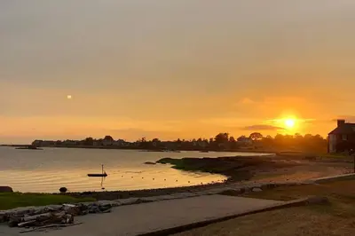 a sunset over a body of water with a boat at Direct Waterfront 4 Bedroom Beach House With Stunning LI Sound Views & Private Beach in Guilford