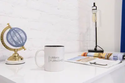 a coffee mug sitting on a white desk with a fan at 240-12 BRAND NEW Studio Prime location W&D in New York