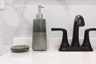 a black soap dispenser sitting next to two faucets at 240-14 NEW Studio Prime Location W&D in unit in New York