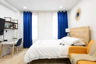 a bedroom with a bed and a desk and blue curtains at 1597-12 NEW Studio Prime UES WD in unit in New York