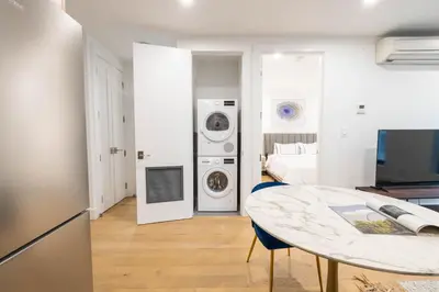 a living room with a table and a room with a bed at 149BK-202 NEW Condo 1BR IN PRIME GREENPOINT BK in Brooklyn