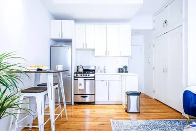 a white kitchen with white cabinets and a table at 62-3B Studio Prime UES Walk to Central Park in New York