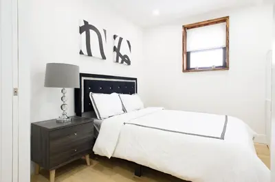 a white bedroom with a bed and a table with a lamp at 75-5D NEW Quality 3BR Duplex W&D Elevator in New York