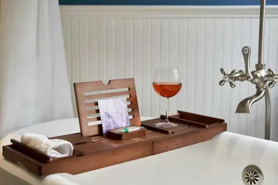 a wooden tray with a glass of wine on a bath tub at Guilford Carriage House at Granite Lodge! in Guilford