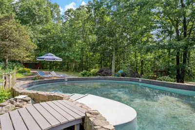 a swimming pool with a bench and an umbrella at Guilford Carriage House at Granite Lodge! in Guilford