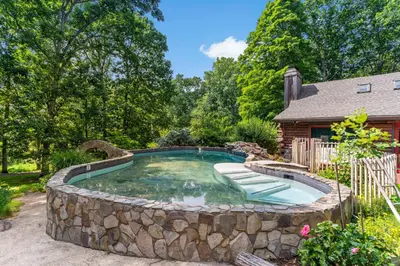 a large pool with a rock wall around it at Guilford Carriage House at Granite Lodge! in Guilford
