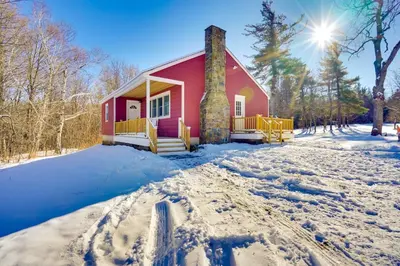a red house in the snow with the sun behind it at Cozy Southern Vermont Home with On-Site Trails in Whitingham