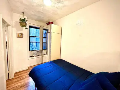 a bedroom with a blue bed in a room with a refrigerator at Bedroom 10 mins to Times Square! and is first floor in Queens