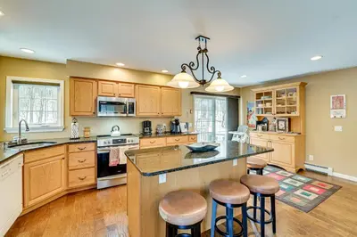 a kitchen with wooden cabinets and a island with bar stools at 5 Mi to Mt Snow West Dover Getaway with Hot Tub in Brattleboro
