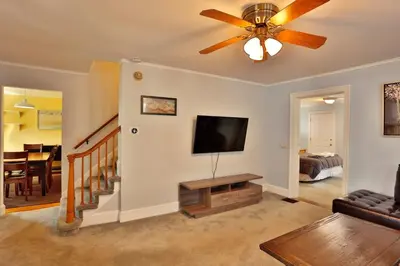 a living room with a ceiling fan and a flat screen tv at The Bullpen All Star Baseball Rentals in Oneonta