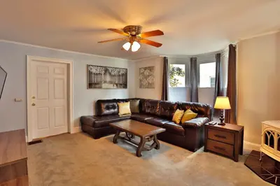 a living room with a leather couch and a ceiling fan at The Bullpen All Star Baseball Rentals in Oneonta