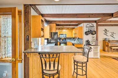 a kitchen with wooden cabinets and a island with two bar stools at Berkshires Getaway Less Than 1 Mi Skiing and Hiking! in Shelburne Falls