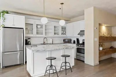 a kitchen with white cabinets and a large island with bar stools at Tribeca Loft Vanderbilt by RoveTravel in New York