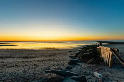 a sunset on a beach with rocks and the ocean at DUNE Fairfield Beach in Fairfield