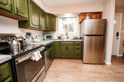 a kitchen with green cabinets and a stainless steel refrigerator at Hot Cocoa Bar 4 Season Porch wWood Stove in Pocono Country Place